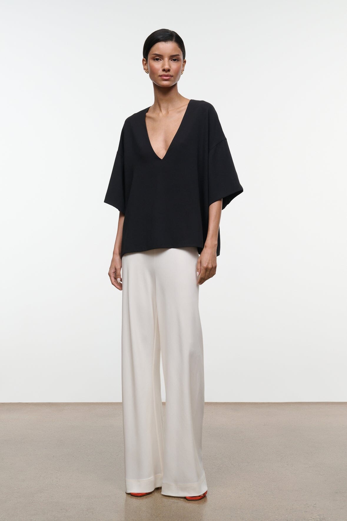 Black studio tee with deep V-neck and wide short sleeves worn with light trousers