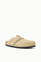 A light beige suede clog-style slip-on shoe with a black sole, shown from a side profile against a plain white background.