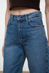 Close-up of a person wearing medium-wash blue denim jeans with a cropped dark brown top visible at the waist.