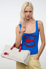 Cream tote bag with red handles and red fish applique, carried in front