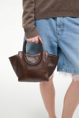 MAUDE mini tote held at side, espresso distressed brown with dual top handles