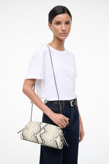 Convertible clutch bag in white snake-print, worn crossbody with adjustable strap