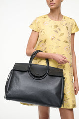Black carryall handbag with curved front flap and side tie accents