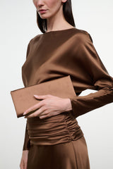 Brown satin clutch in hand with draped long-sleeve dress, ruched waist.
