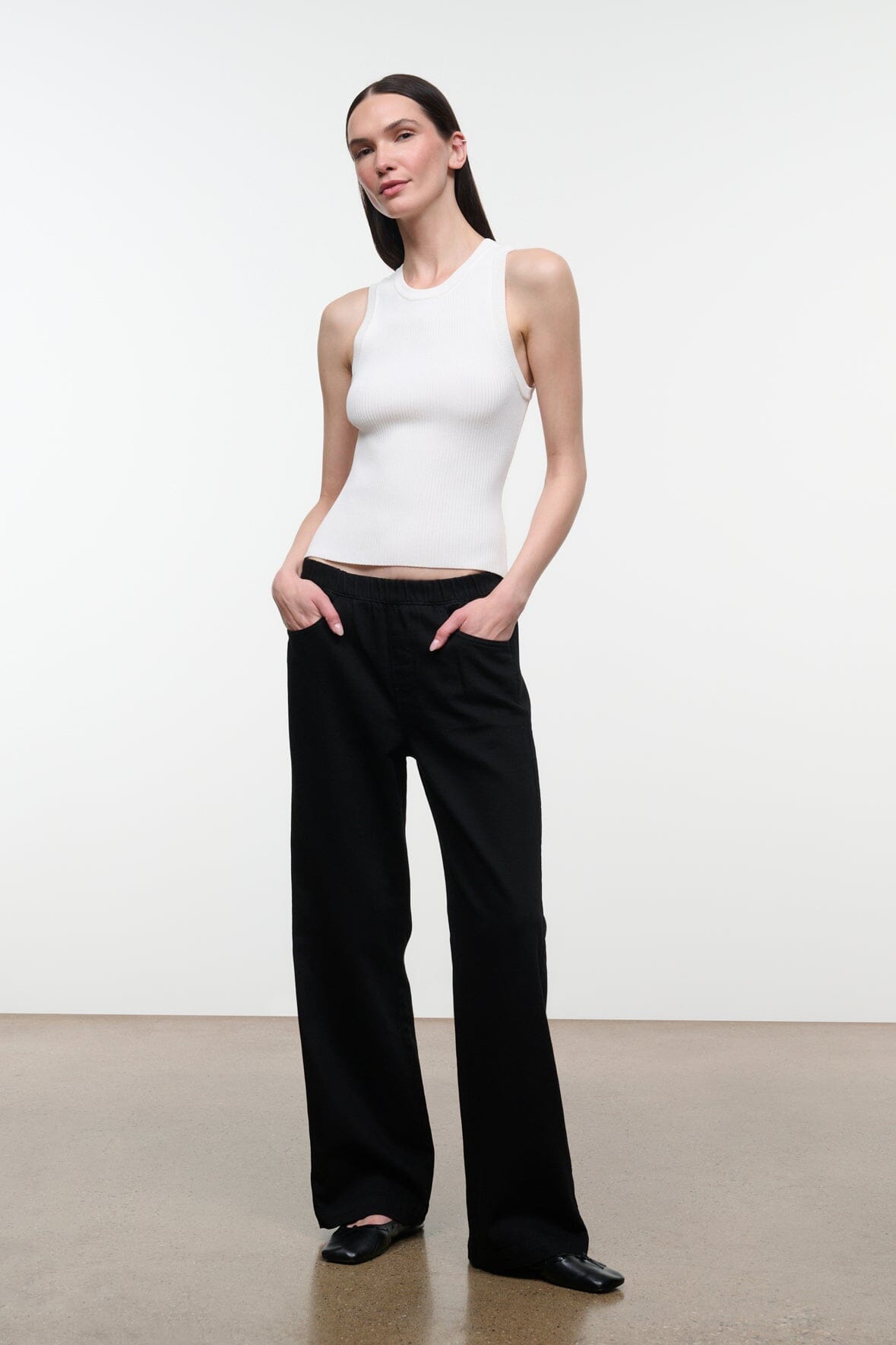 A woman modeling a white sleeveless ribbed tank top and black wide-leg trousers against a clean white studio background.