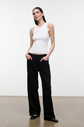 A woman modeling a white sleeveless ribbed tank top and black wide-leg trousers against a clean white studio background.
