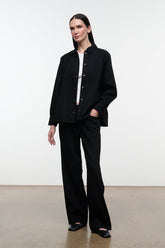 Black shirt jacket over black pants, stand collar and button front; standing full-body view.