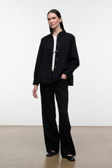 Black shirt jacket over black pants, stand collar and button front; standing full-body view.