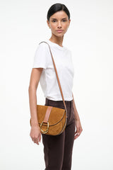 Tan suede saddle bag worn crossbody, foldover flap with gold ring hardware.