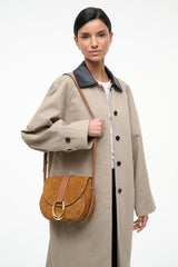 Tan suede saddle bag worn crossbody on flap with gold ring and leather strap.