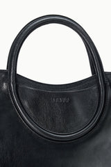 Maude black satchel close-up: oval handle base with stamped logo