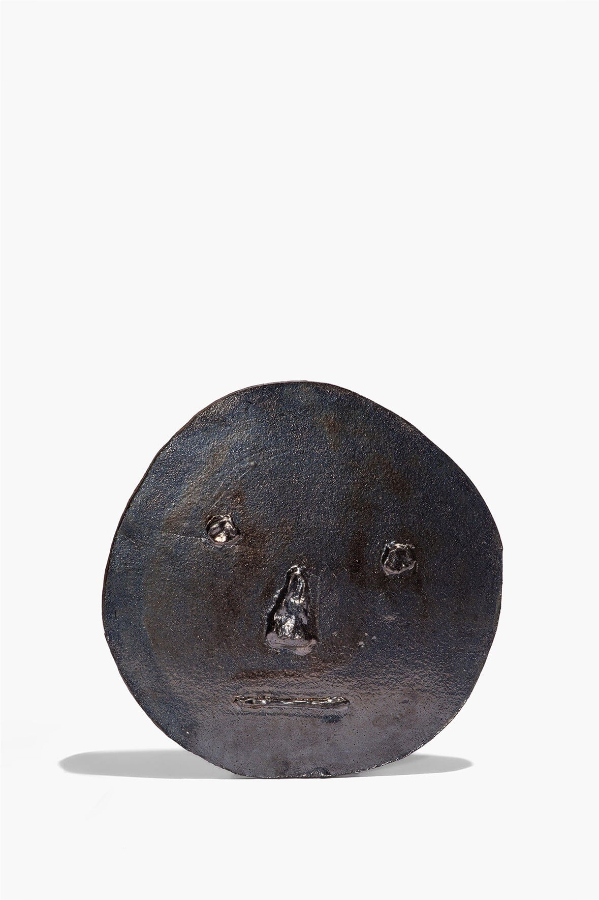 Round ceramic face ornament in dark burnt black glaze, embossed eyes and nose