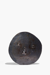 Round ceramic face ornament in dark burnt black glaze, embossed eyes and nose