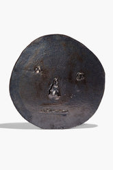 Ceramic face ornament in dark burnt black glaze, round with embossed facial features