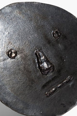 Round ceramic face ornament close-up in dark burnt black glaze with embossed details