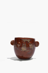 Ceramic candle pot with brown glaze, side handles, and raised face features; open top