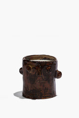 Brown ceramic candle holder with sculpted face, circular side details, open top