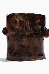 Brown ceramic candle holder with sculpted face and side knobs, wide open top