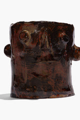 Brown ceramic candle holder with sculpted face and side knobs, wide open top
