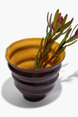 Stacked cone vase holding red and green flower stems, mustard interior