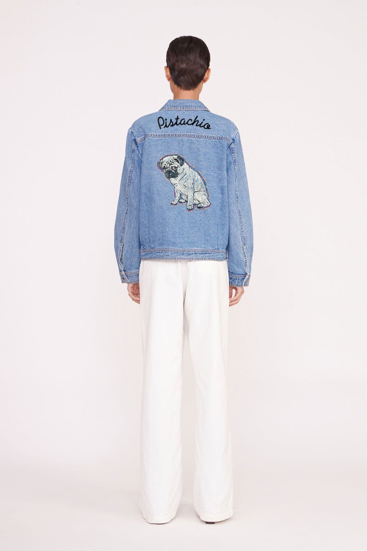 Medium-wash denim jacket back view with dog patch and 'Pistachia' lettering