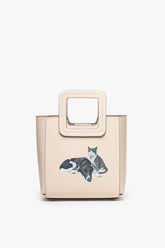 Cream mini leather bag with framed handle and cat pet graphic.