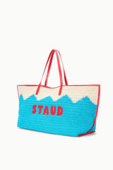 Blue crocheted tote bag with cream top and red handles, “STAUD” text on front