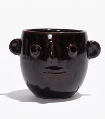 Ceramic candle pot with dark glossy finish and carved smiling face; side handles