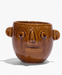 Ceramic candle pot with warm brown glaze and carved smile; circular eye details and handles