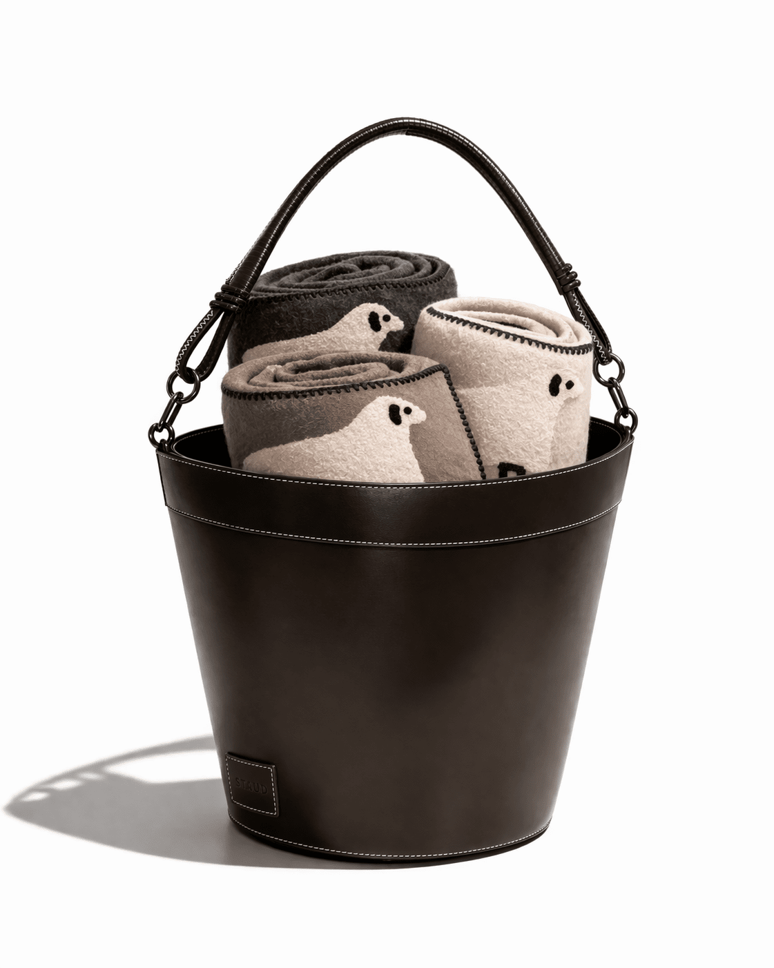 Dark brown leather bin with handle holding folded towels, visible inner lining and stitched base.