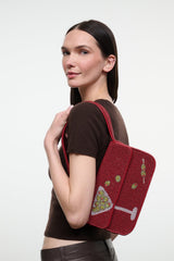 Red beaded handbag with top handle and front flap, shown in profile on a model