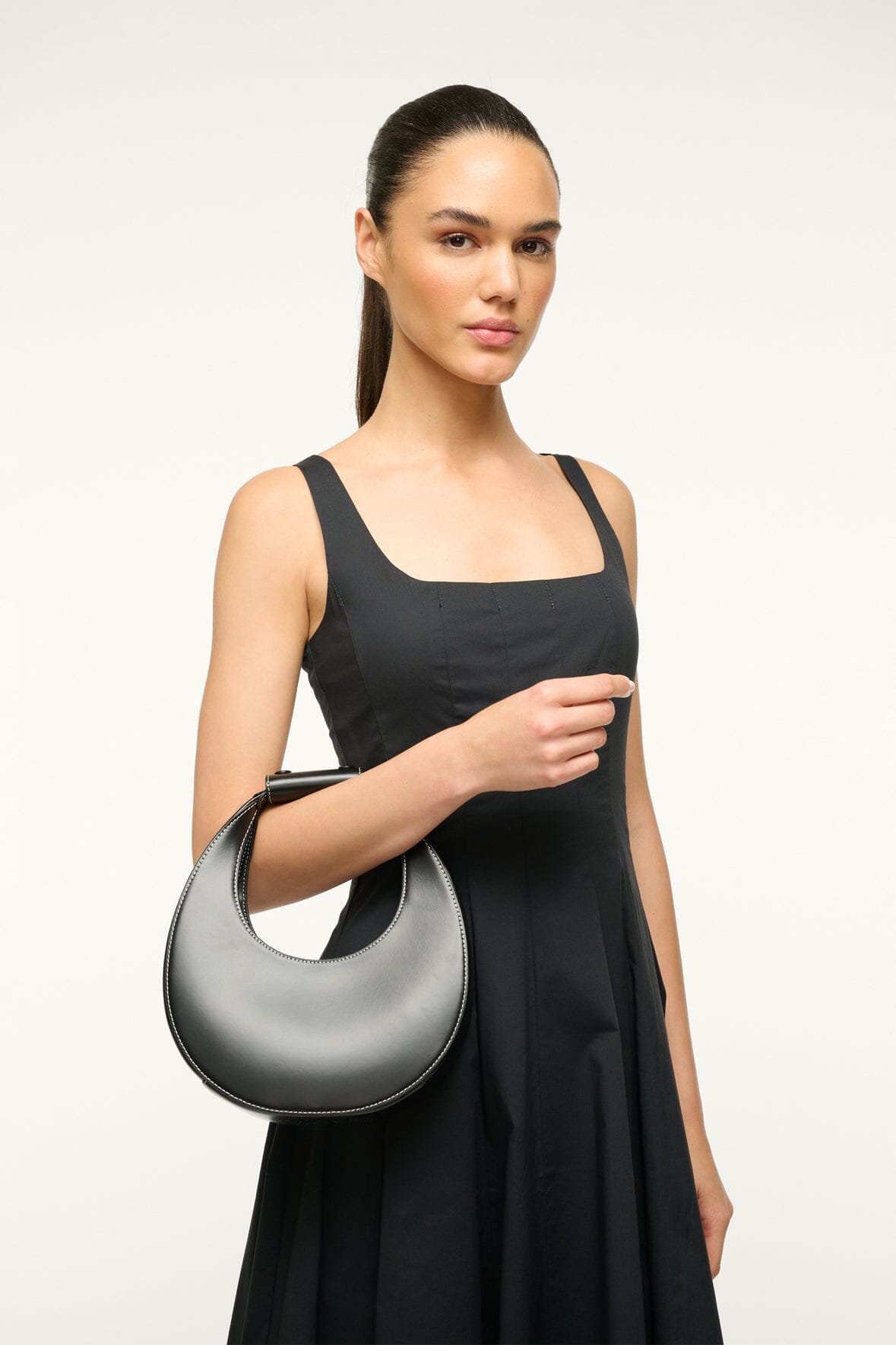 Black mini moon bag held at side with curved top and strap