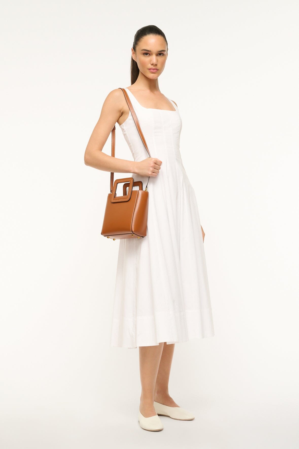 Saddle brown mini leather top-handle bag worn across the body with front clasp