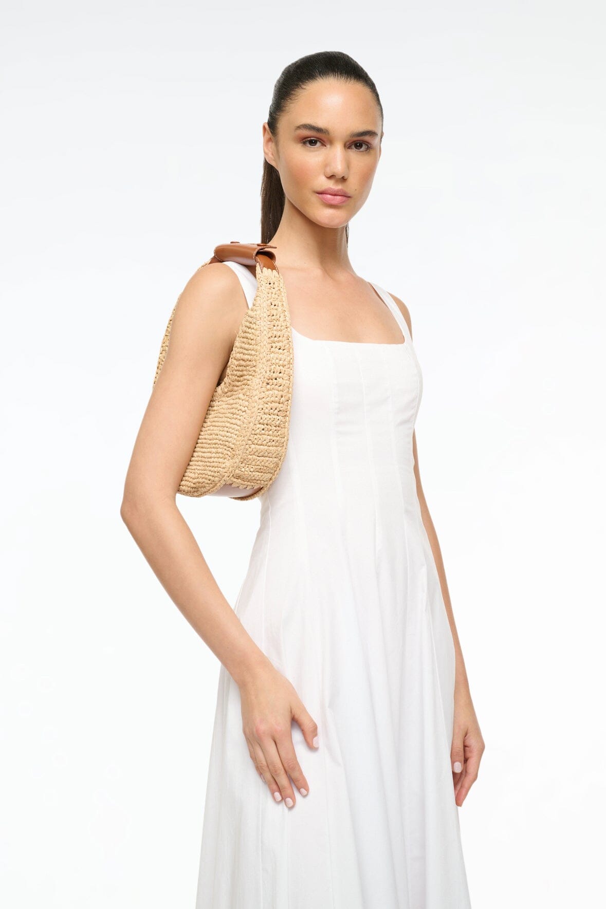 Natural raffia crescent bag with brown leather handle strap, held at side