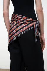 Silk scarf with multicolor geometric stripe pattern, tied at waist over dark pants
