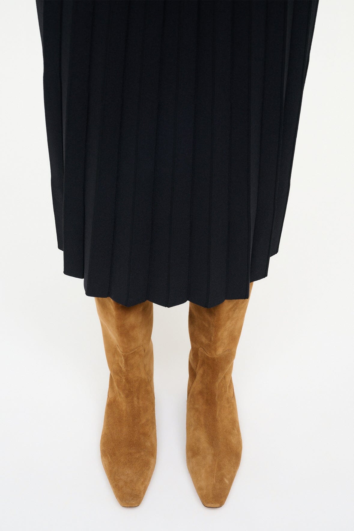 Tan suede flat boots with pointed toe and dark low heel beneath black skirt
