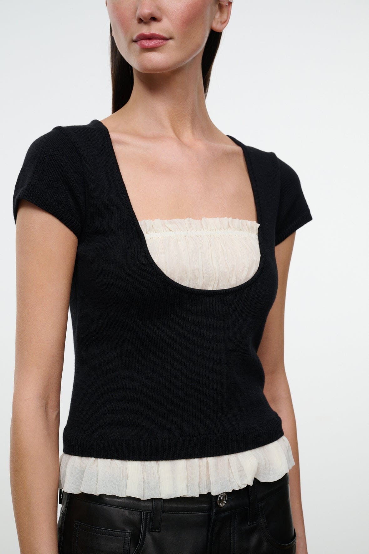 Black knit top with scoop neckline and ivory ruffled trim at hem