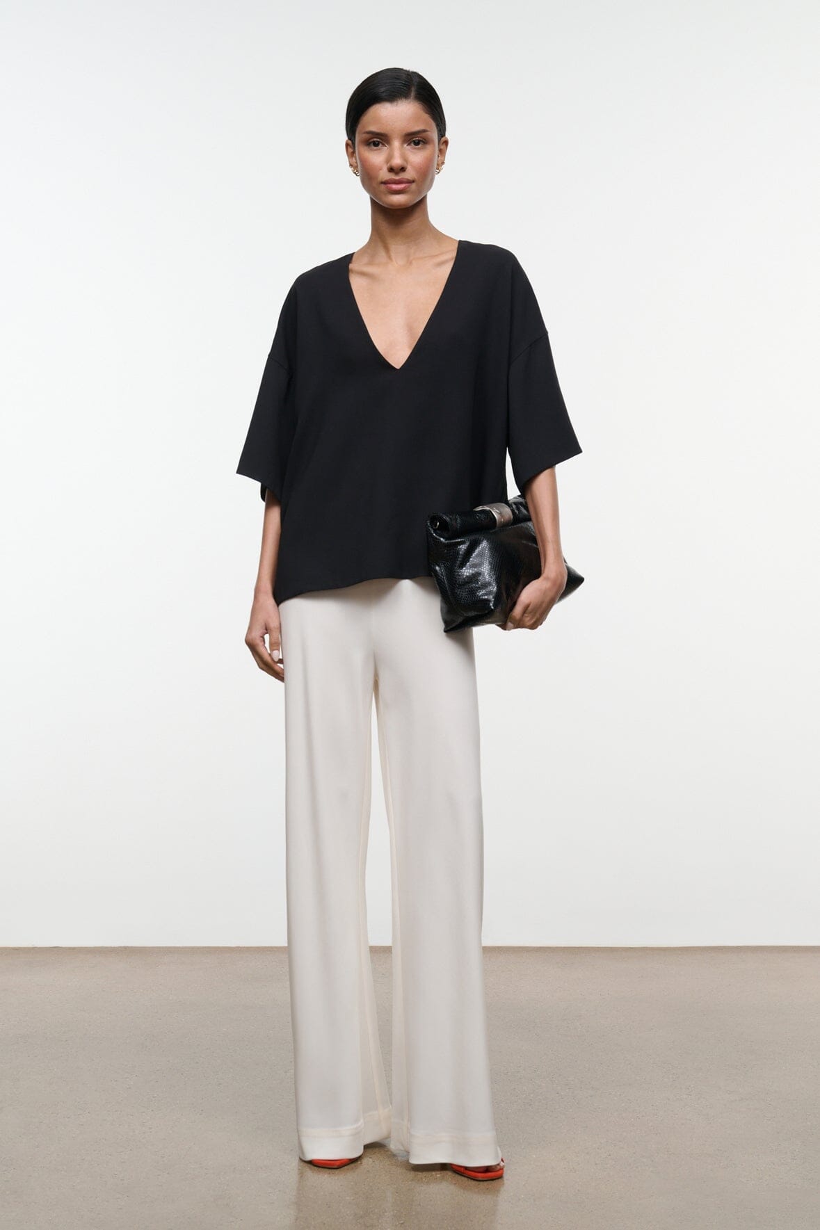 Black studio tee with deep V-neckline and loose short sleeves worn with light trousers