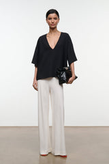 Black studio tee with deep V-neckline and loose short sleeves worn with light trousers