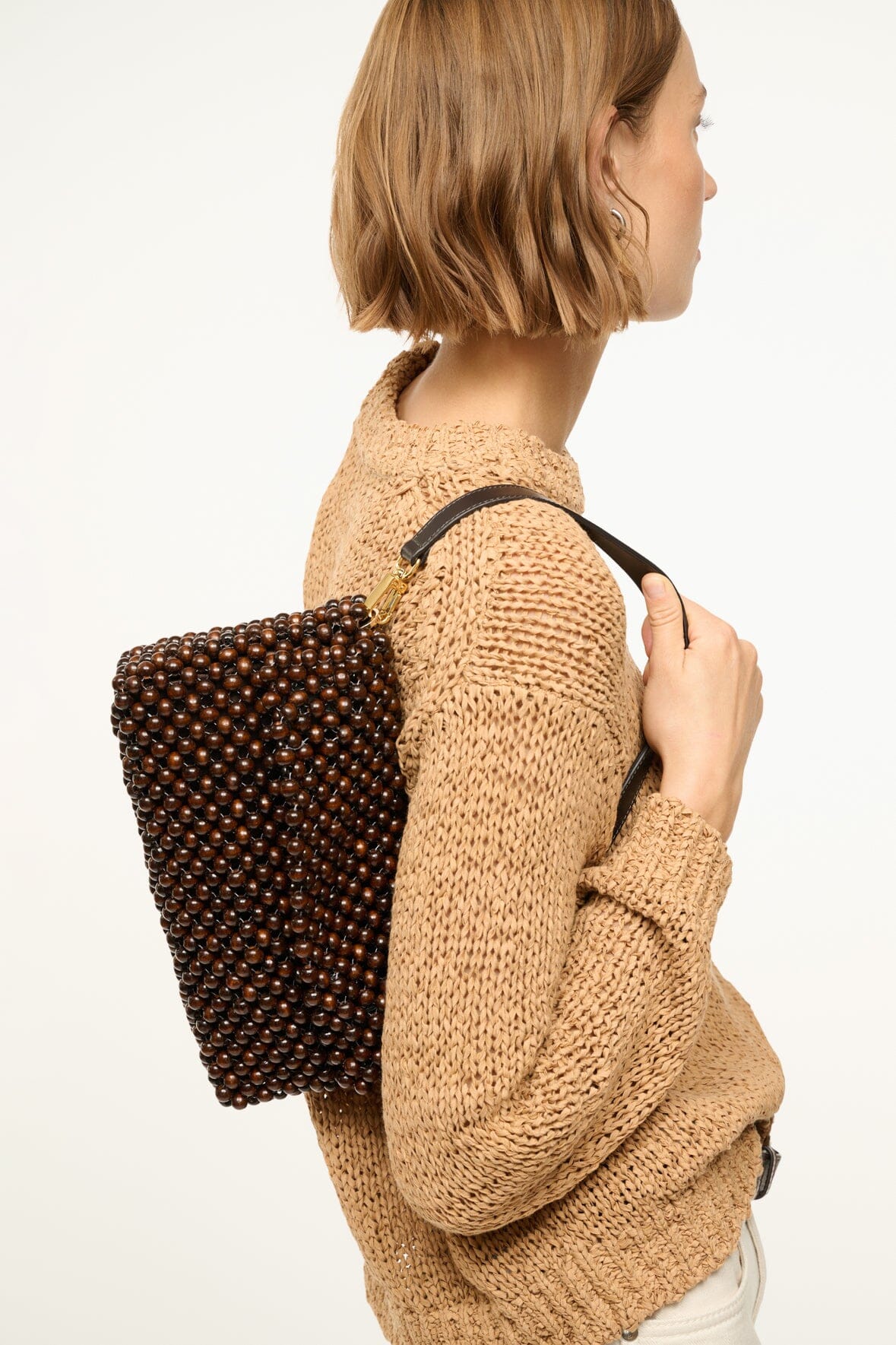 Dark brown beaded shoulder bag viewed from the side, model holding by strap