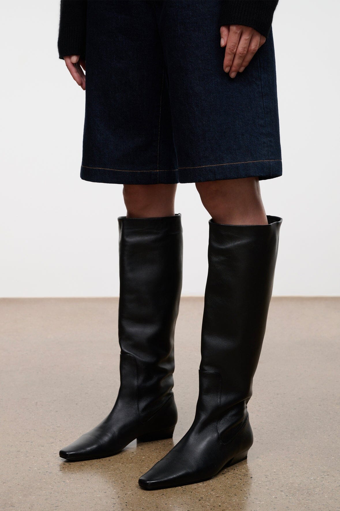 Black knee-high flat pull-on boots with smooth leather-like finish