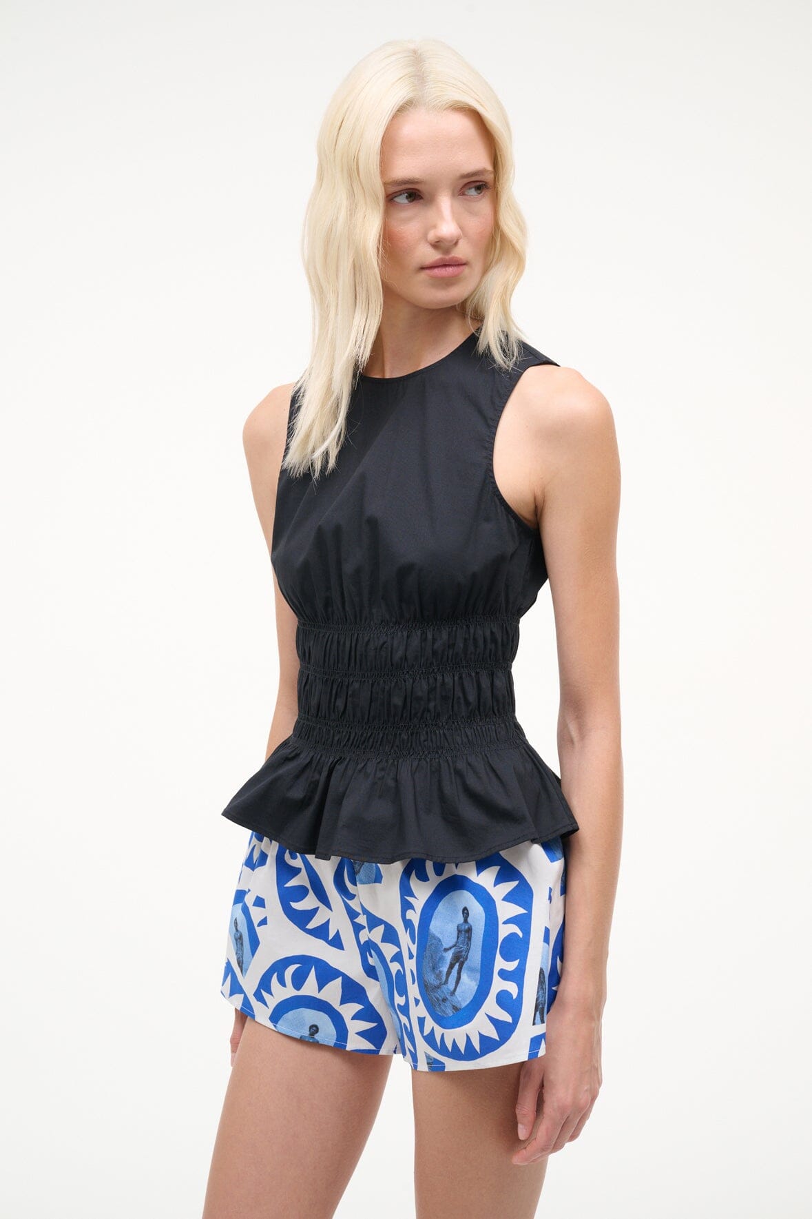 Black sleeveless peplum top with smocked waist and round neckline.