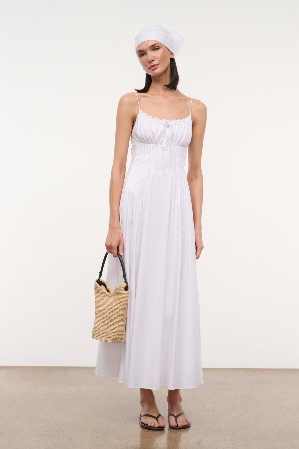 White spaghetti-strap maxi dress with gathered bust, worn with straw bag