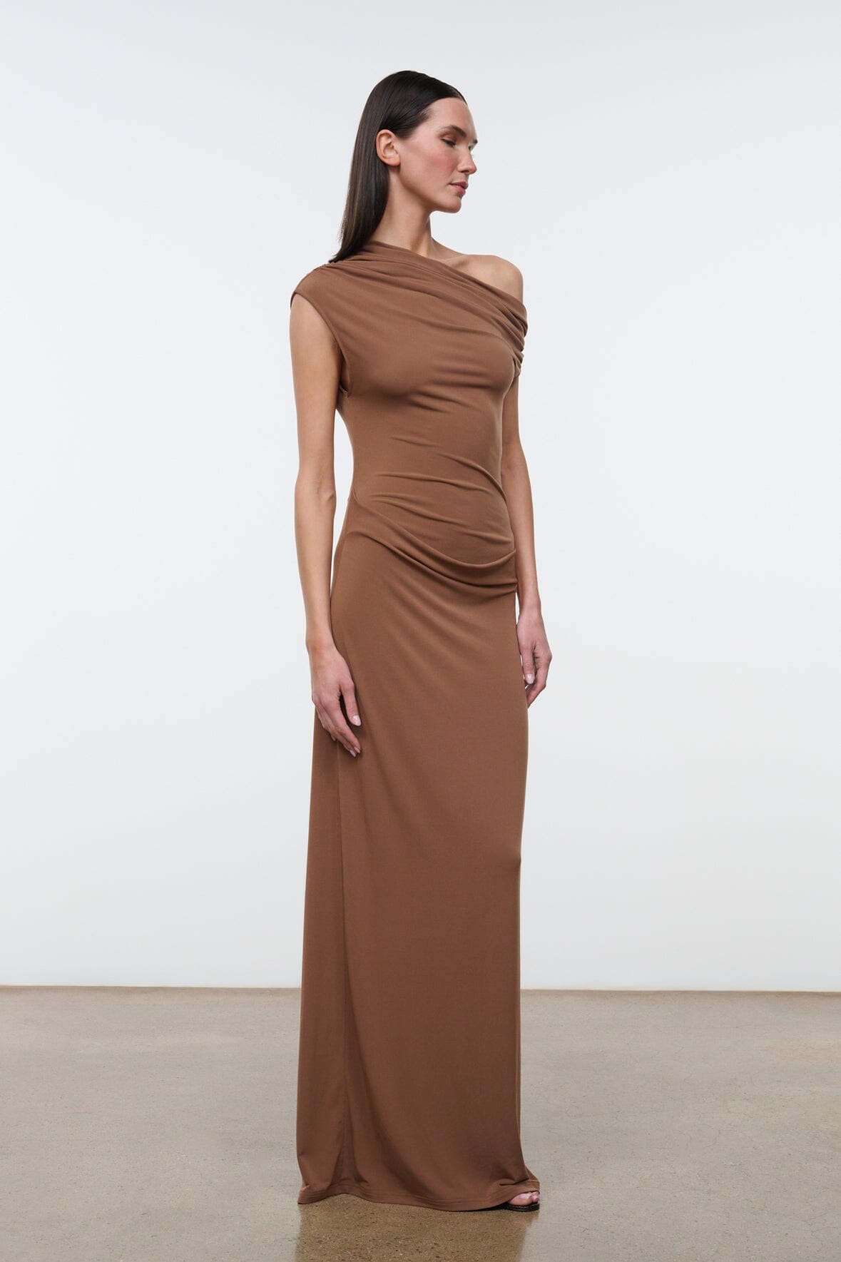 Women's draped one-shoulder maxi dress in warm brown, side view with gathered detail.