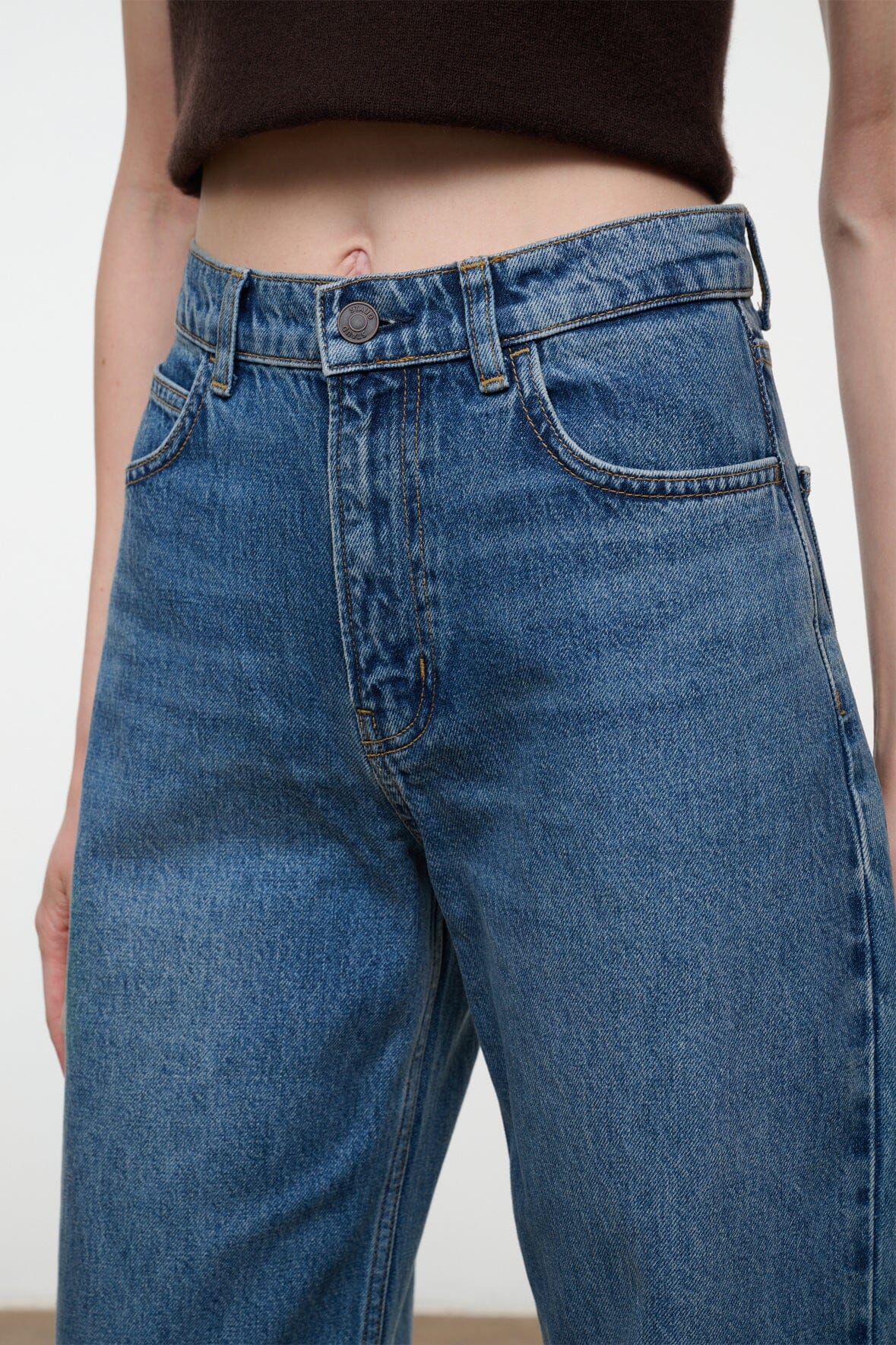 Close-up of a person wearing medium-wash blue denim jeans with a cropped dark brown top visible at the waist.