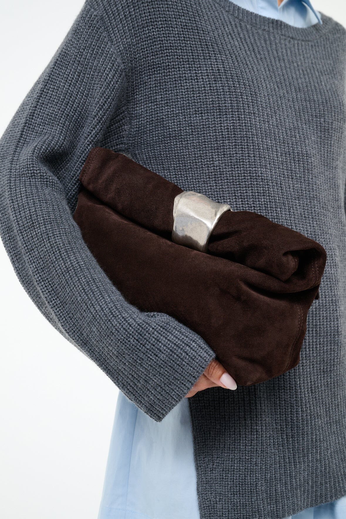 Espresso suede cuff clutch with silver-tone clasp, held in hand