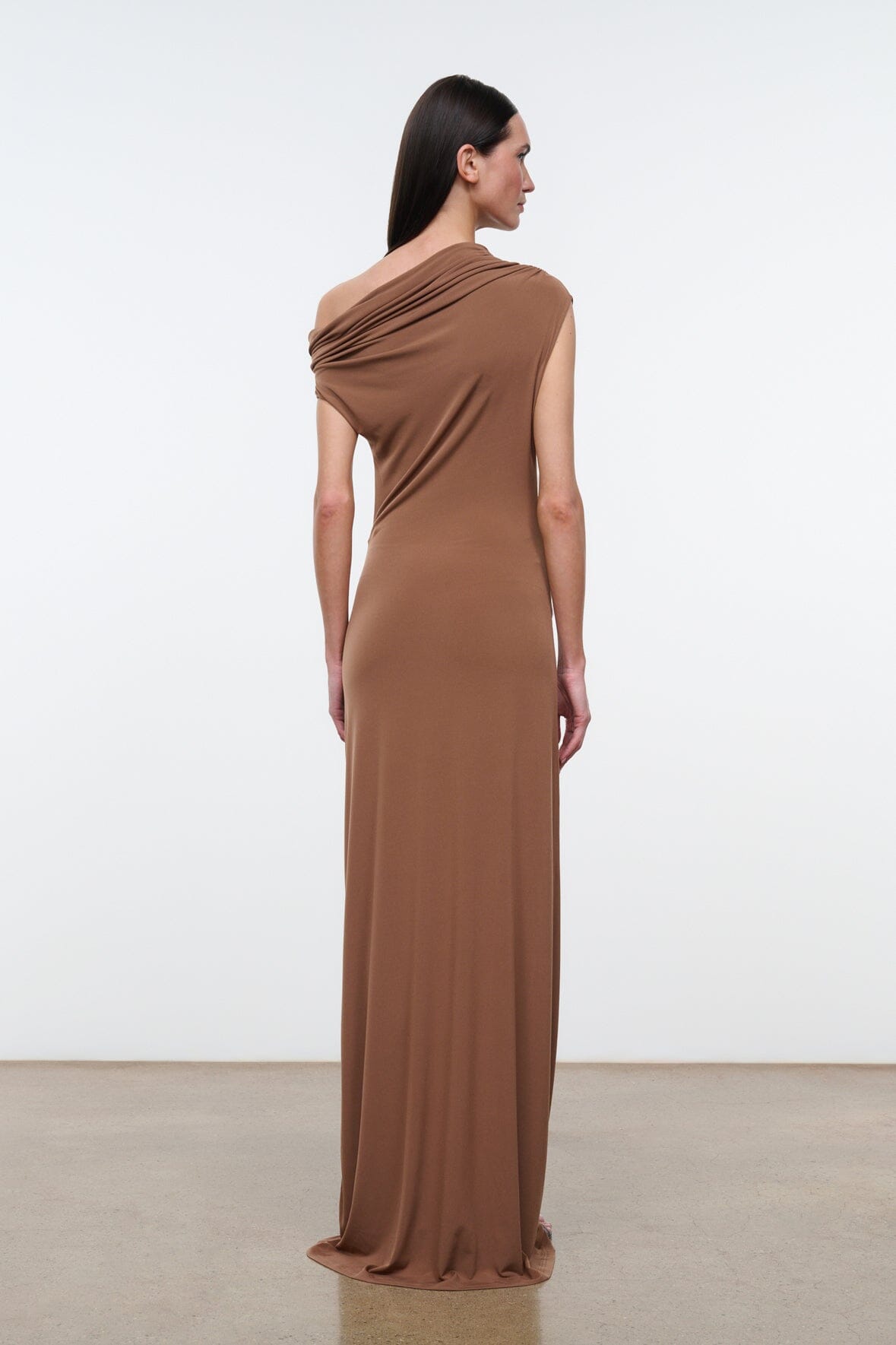 Women's draped one-shoulder maxi dress in warm brown, back view with diagonal drape.