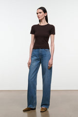 A woman modeling a dark brown short-sleeve crewneck t-shirt and wide-leg blue jeans, standing against a plain white studio background.