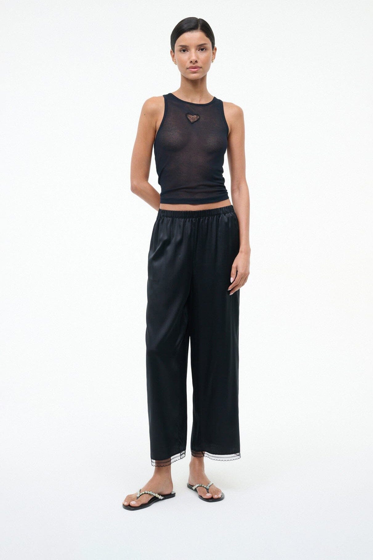 Pearl-beaded black thong sandals on a model with dark wide-leg pants.