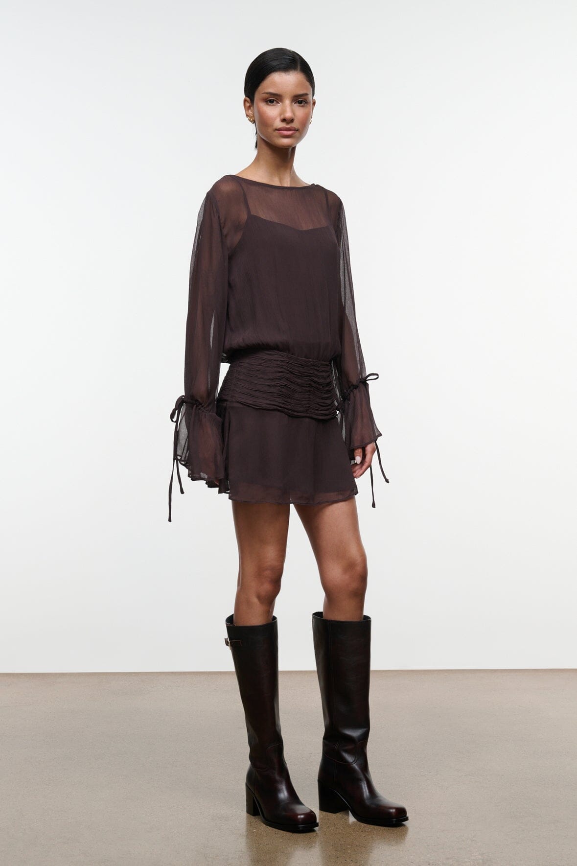 Dark brown sheer long-sleeve mini dress with ruched waist and hanging tie-cuff details.